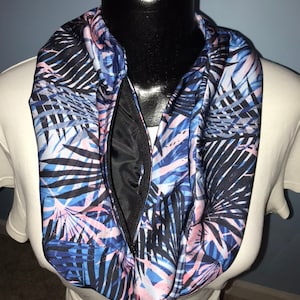 May include: A blue, pink, and black infinity scarf with a zipper closure. The scarf features a tropical leaf pattern.