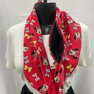 May include: Red infinity scarf with a black zipper and a Minnie Mouse print. The scarf features a repeating pattern of Minnie Mouse's face with a yellow bow.