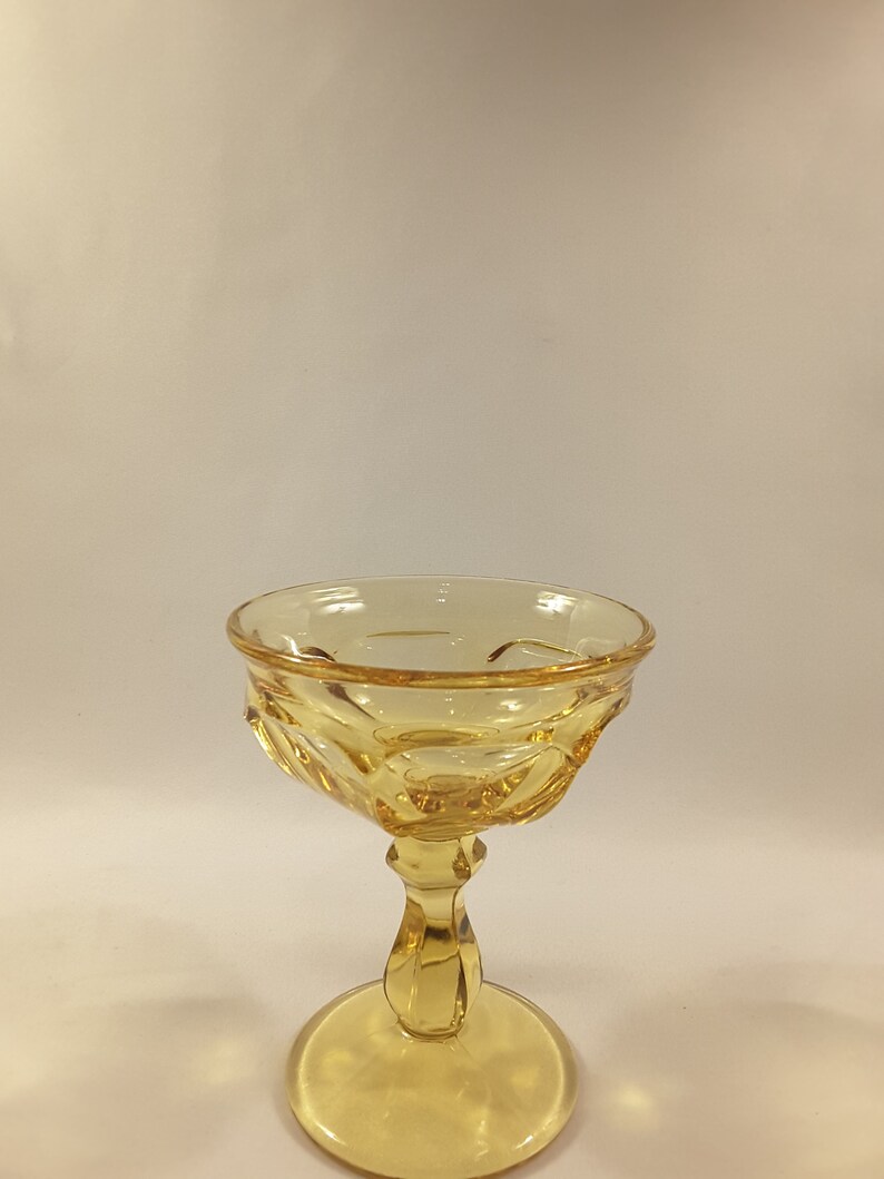 May include: A yellow glass goblet with a fluted bowl and a short stem. The goblet has a wide base.
