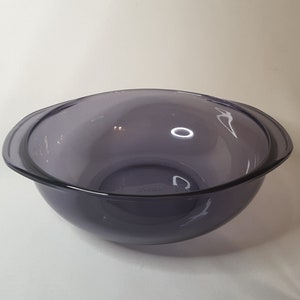 May include: A large, clear, purple glass mixing bowl with two handles. The bowl is empty and sitting on a white surface.