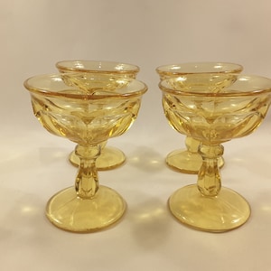 May include: Four amber-colored glass champagne coupes with a fluted design. The coupes have a short stem and a round base.
