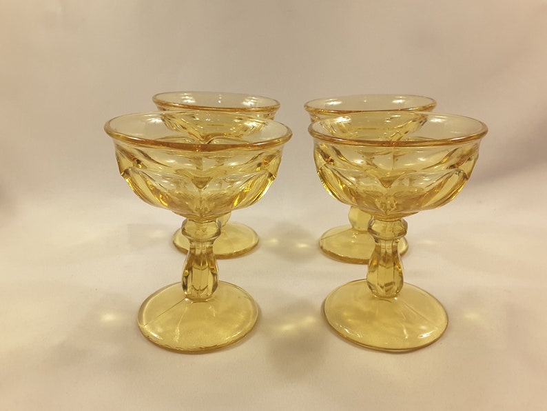 May include: Four amber-colored glass champagne coupes with a fluted design. The coupes have a short stem and a round base.