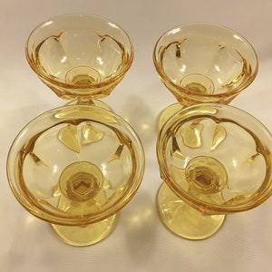 May include: Four amber-colored glass dessert cups with a fluted design. The cups are empty and have a clear, shiny finish.