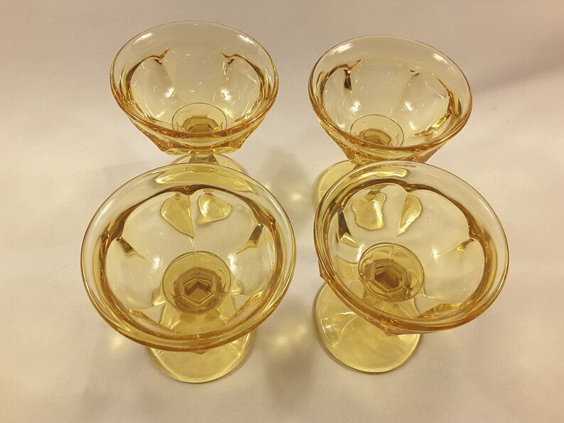 May include: Four amber-colored glass dessert cups with a fluted design. The cups are empty and have a clear, shiny finish.