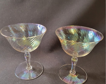 May include: Two iridescent glass cocktail glasses with a swirl design. The glasses have a clear base and a wide, shallow bowl.