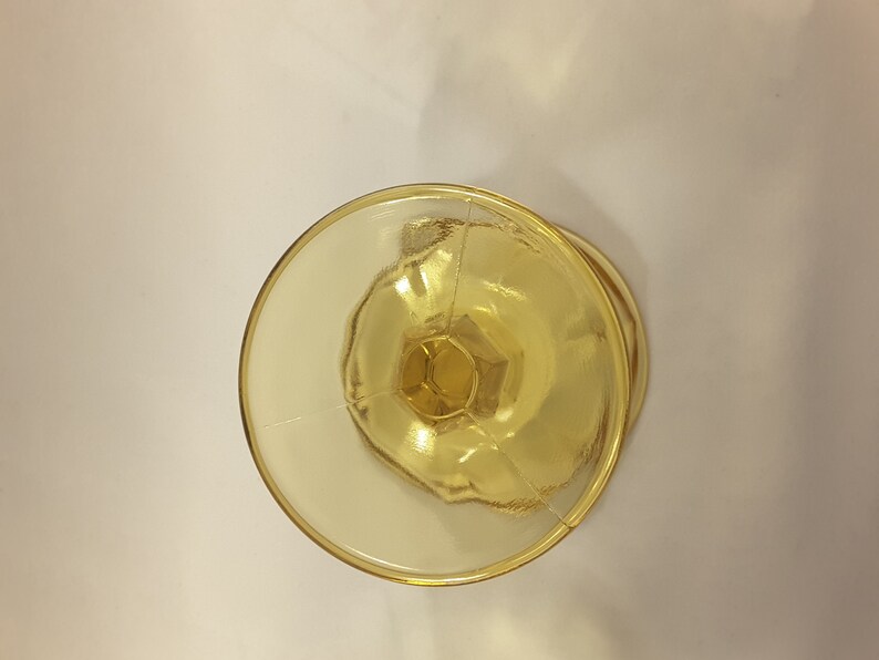 May include: A clear yellow glass goblet with a fluted design. The goblet is empty and has a round base.