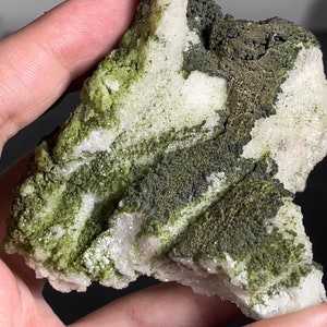 May include: A rough, white and green rock with a dark gray mineral vein. The rock has a rough, textured surface.