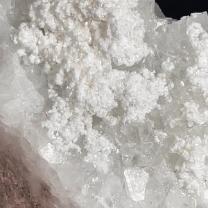 May include: A cluster of white calcite crystals with a rough, natural texture. The crystals are translucent and have a slightly iridescent sheen.