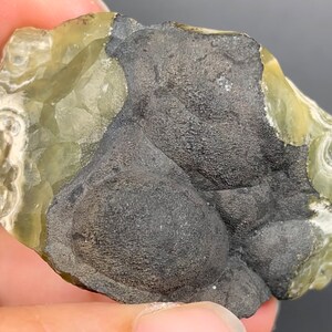 May include: A close-up of a green and black rock with a rough texture. The rock has a smooth, shiny surface on one side and a rough, textured surface on the other side.