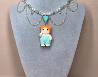 Könnte beinhalten: Eine skurrile Halskette mit einer kleinen orange-weiß-farbenen Tierfigur in blauen Overalls. Die Halskette hat eine Perlenkette mit Perlen und türkisfarbenen Perlen, mit silbernen Kettenakzenten und einem türkisfarbenen Herzanhänger.