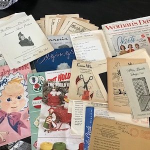 May include: A collection of vintage craft and sewing pattern booklets, including titles like Your Baby Book, Woman's Day, and American Home Pattern. The assortment features various paper pamphlets with illustrations, text, and handwritten notes.
