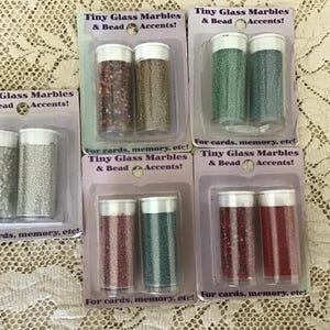 May include: Five blister packs of Tiny Glass Marbles & Bead Accents, each containing two clear plastic tubes filled with small decorative beads in various colors including silver, brown, gold, green, teal, and red, with white caps.