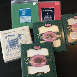Peut inclure: Assortiment de tissus Aida pour des projets de point de croix. Les emballages sont verts et blancs avec le logo Charles Craft et le texte "Cross Stitch Fabric". Un emballage présente un dessin de calèche bleu.