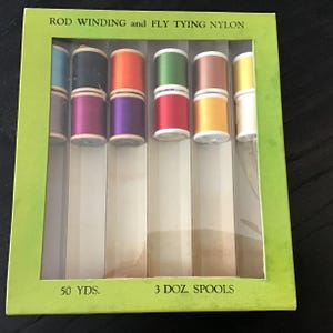 May include: A package of nylon thread spools for rod winding and fly tying. The spools are in various colors, including orange, green, and yellow. The package is green and has text that reads "ROD WINDING and FLY TYING NYLON".