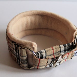 Puede incluir: Un collar acolchado para perros, beige y a cuadros. El collar tiene un interior suave de color beige y un exterior a cuadros en beige, negro y rojo. Cuenta con anillos de metal plateado y una hebilla.