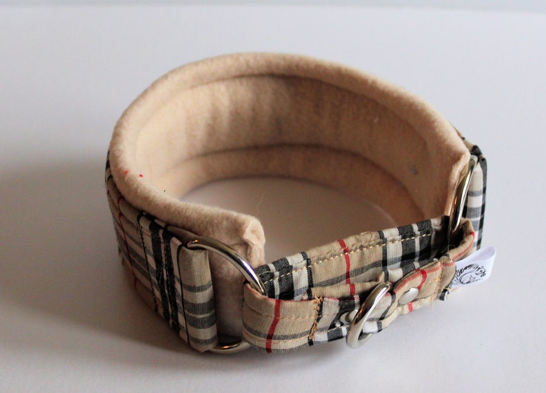Puede incluir: Un collar acolchado para perros, beige y a cuadros. El collar tiene un interior suave de color beige y un exterior a cuadros en beige, negro y rojo. Cuenta con anillos de metal plateado y una hebilla.