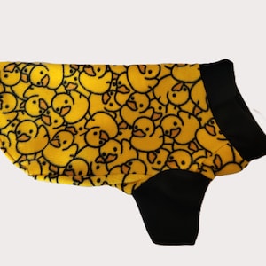 May include: Yellow dog coat with a repeating pattern of cartoon duck faces outlined in black. The coat has black sleeves and a black collar. This dog coat is designed to keep a dog warm and comfortable.