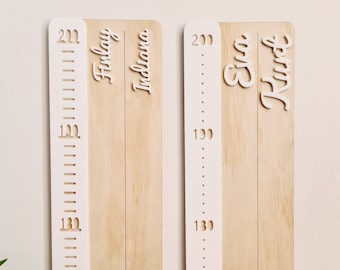 May include: Two wooden growth charts with white numbers and names. The chart on the left reads "Finlay Indiana" and the chart on the right reads "Eva Kirst".