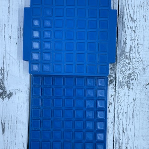May include: Two blue plastic mats with a grid of square indentations. The mats are designed for use with small objects, such as beads or dice.
