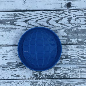 May include: A blue silicone mold shaped like a globe with a grid pattern. The mold is on a white wooden surface.