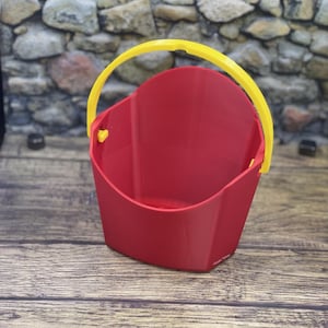 May include: A red plastic bucket with a yellow handle. The bucket is designed to hold small items, such as toys or snacks.