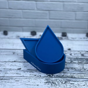 May include: A set of three blue silicone molds shaped like a teardrop, a triangle, and a half-circle. The molds are stacked on top of each other. The text "© Kinder Things" is visible on the bottom mold.