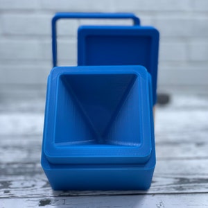 May include: Three blue plastic containers with a square shape and a funnel-shaped top. The containers are stacked on top of each other.