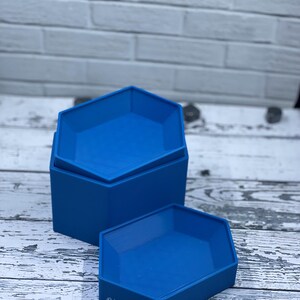 May include: Two blue hexagonal stacking trays. The trays are made of a smooth plastic and are perfect for organizing small items.