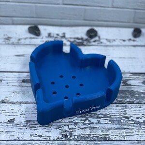 May include: A blue silicone heart-shaped ashtray with drainage holes and the text "© KINDER THINGS" on the bottom.
