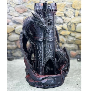 May include: A black dragon sculpture wrapped around a castle tower. The tower has arched windows and a detailed design. The dragon's wings are spread, and the base has a red accent. The sculpture is set against a stone wall background.