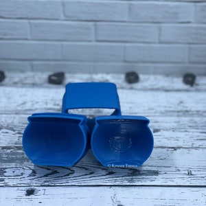May include: Three blue plastic cookie cutters shaped like a pot. The cookie cutters are on a white wooden surface.