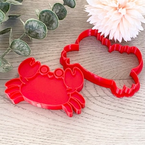 May include: Two red plastic cookie cutters, one shaped like a crab and the other shaped like a cloud.