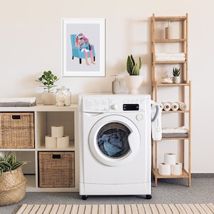 May include: A white washing machine with a glass door and a digital display. The washing machine is in a laundry room with a white shelf unit, a bamboo shelf unit, and a framed print of a person sitting in a chair.
