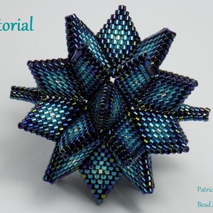 Pode incluir: Um ornamento de contas em forma de estrela azul e verde iridescente. O ornamento é feito de pequenas contas quadradas que são costuradas juntas em um padrão complexo. O ornamento é um tutorial do Bead Mechanics.