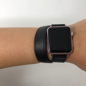May include: A black leather Apple Watch band with a rose gold Apple Watch. The band is double-wrapped around the wrist.