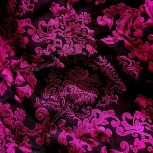 Pu&ograve; includere: Primo piano di un tessuto lussuoso con sfondo scuro e un vivace motivo floreale magenta. Il design presenta dettagli intricati e vorticosi, creando un aspetto ricco e strutturato. La lucentezza del tessuto suggerisce un materiale di alta qualit&agrave;, adatto all'abbigliamento o all'arredamento.