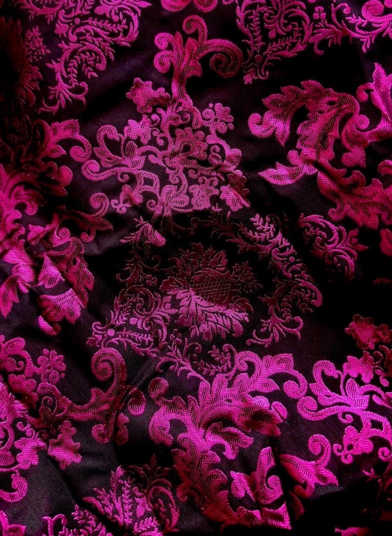 Pu&ograve; includere: Primo piano di un tessuto lussuoso con sfondo scuro e un vivace motivo floreale magenta. Il design presenta dettagli intricati e vorticosi, creando un aspetto ricco e strutturato. La lucentezza del tessuto suggerisce un materiale di alta qualit&agrave;, adatto all'abbigliamento o all'arredamento.