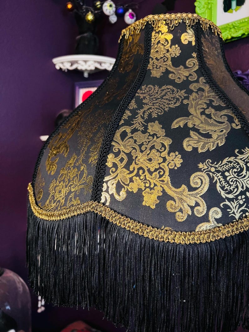 Pu&ograve; includere: Paralume nero con motivo floreale dorato e frange. Il paralume ha un bordo dorato e frange nere sul fondo. Un elemento di illuminazione decorativo.