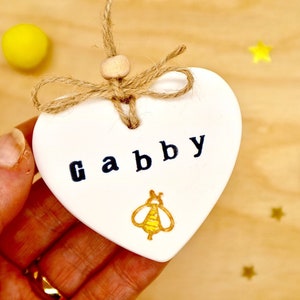 Personalised bee keepsake decoration, handmade from white clay, with a gold and yellow stamped bee. A hanging heart for birthdays or any other occasion. Tied with natural jute twine and wooden bead. Gift for friend, daughter, girl, mum.