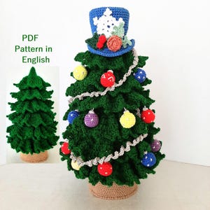 Puede incluir: Un árbol de Navidad verde tejido a mano, decorado con adornos coloridos y un sombrero de copa azul. El árbol está adornado con adornos rojos, amarillos, morados y azules. El árbol está en una cesta tejida. El texto "PDF Pattern in English" está en la imagen.