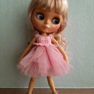 May include: A pink crocheted bodice and tulle skirt doll dress. The doll has blonde hair and blue eyes.