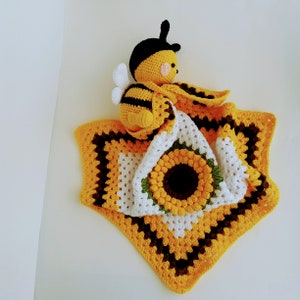 Puede incluir: Una manta de bebé de ganchillo con un diseño de abeja amarilla y marrón y un girasol.