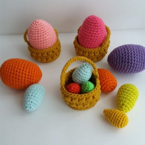 May include: A collection of crocheted Easter eggs in various colors, including pink, orange, purple, green, and blue, are displayed in small crocheted baskets. Some eggs are in baskets, while others are loose.