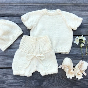 Puede incluir: Un conjunto de punto para beb&eacute; en color crema, que incluye un gorro, un jersey, unos pantalones cortos y unas botitas.