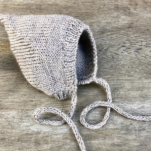 Peut inclure: Un bonnet de bébé en tricot gris avec un sommet pointu et une longue cravate. Le bonnet est fait d'un fil doux et texturé.