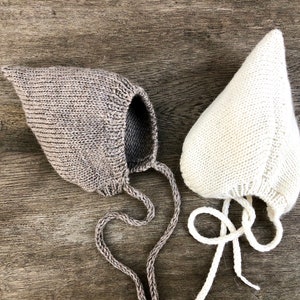 May include: Two knitted baby bonnets with ties. One bonnet is brown and the other is white.