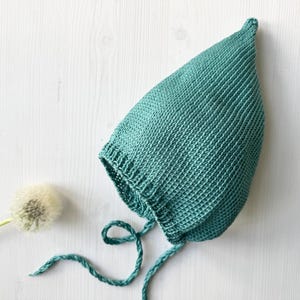 Puede incluir: Un gorro de bebé de punto de color turquesa con lazos. El gorro está hecho de un hilo suave y texturizado y tiene una parte superior puntiaguda.