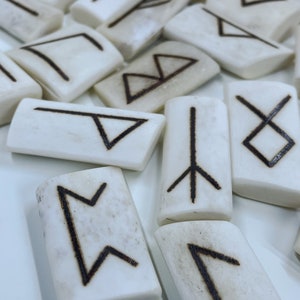 May include: White rectangular tiles with black runes carved into them. The runes are from the Elder Futhark alphabet.