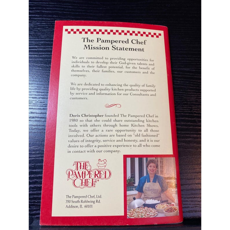 May include: A red and white brochure with "The Pampered Chef Mission Statement" printed on the front. The brochure includes text about the company's values and founder, Doris Christopher. A photo of a woman in an apron is also included.
