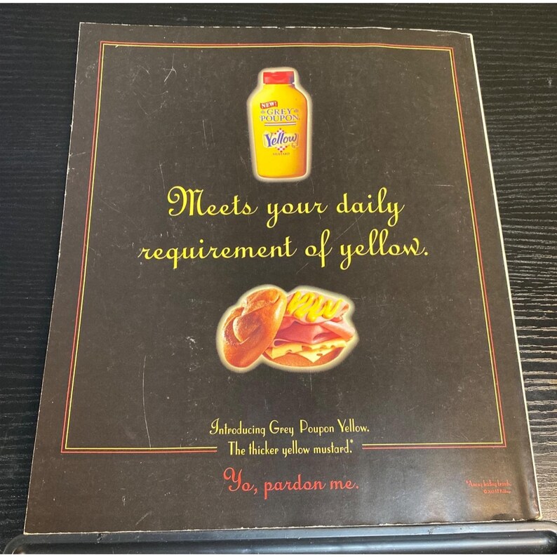 May include: An advertisement for Grey Poupon Yellow mustard. The image features a yellow mustard bottle, a sandwich, and text that reads "Meets your daily requirement of yellow." and "Introducing Grey Poupon Yellow. The thicker yellow mustard."